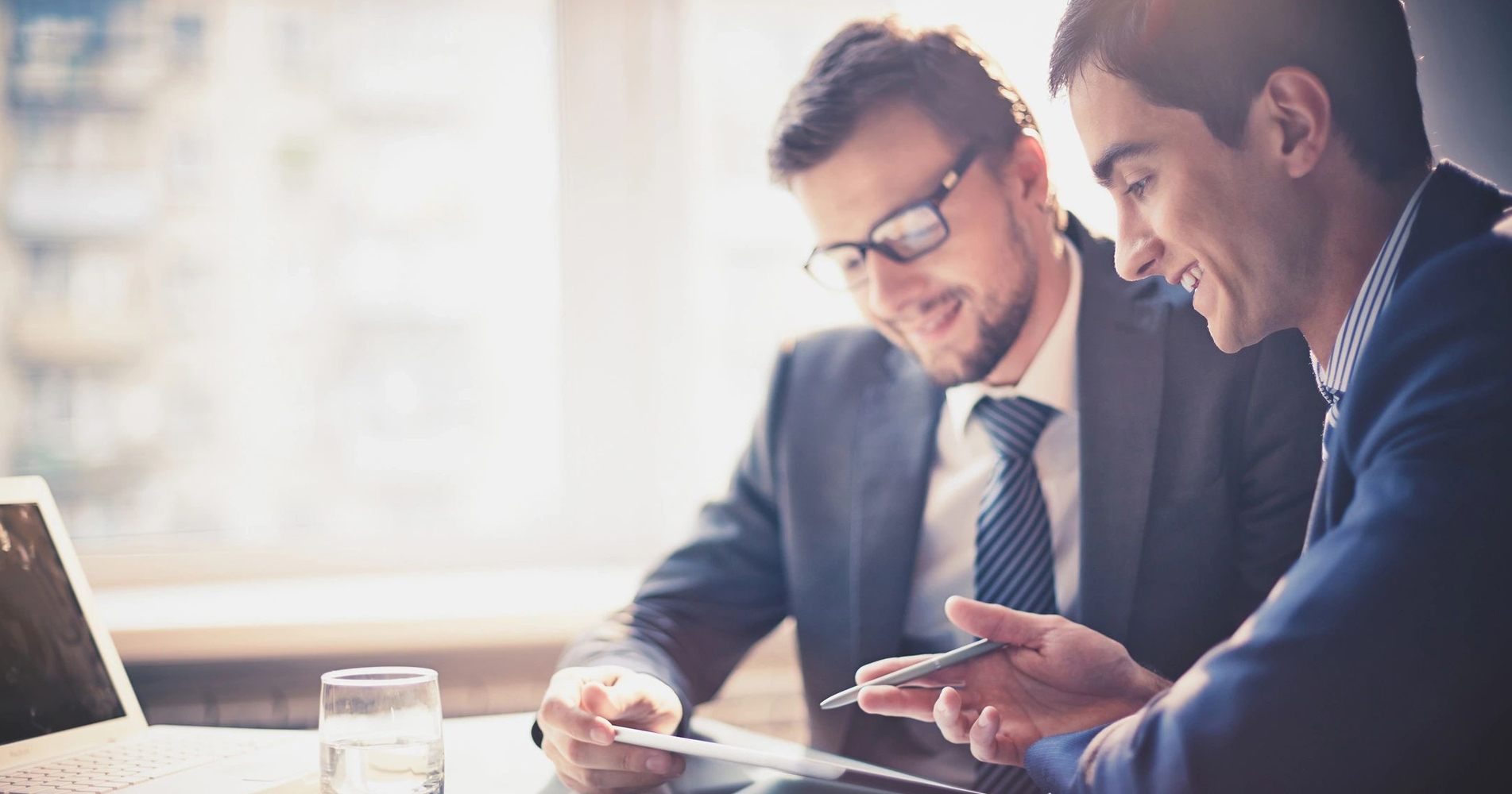 Two men in suits and ties looking at a tablet.